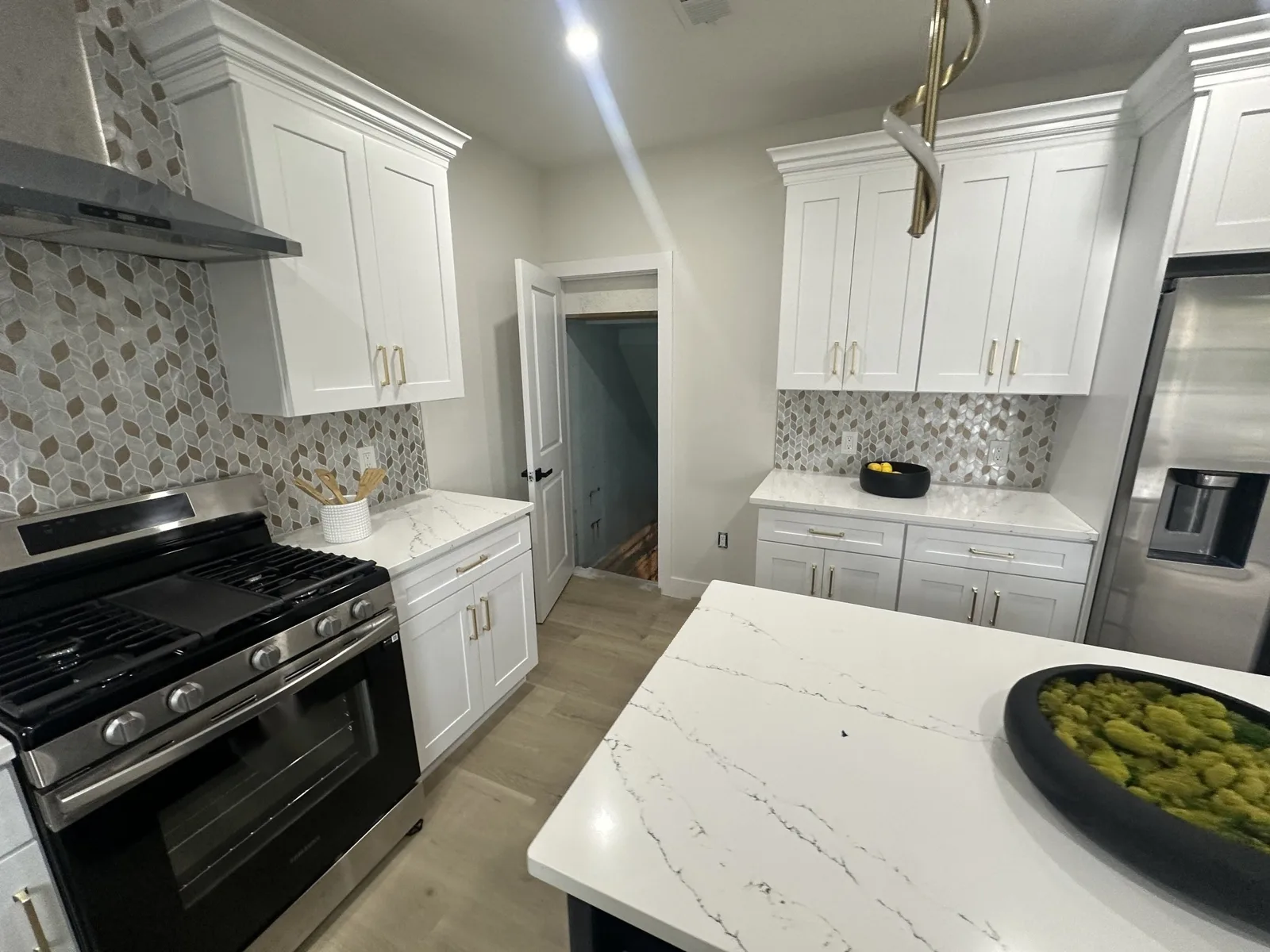 Kitchen with white shaker cabinets and gold pulls, mosaic backsplash, stainless range and refrigerator, and a white stone-look island