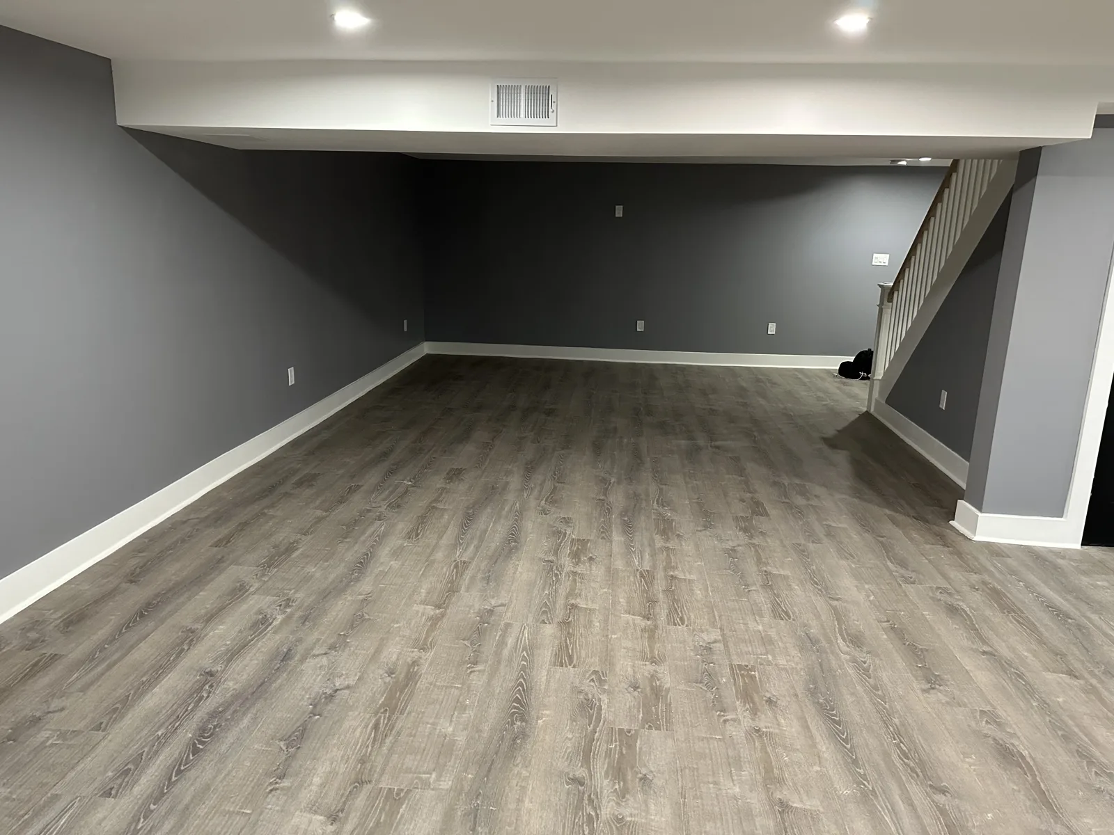 Finished basement with gray walls, white trim, recessed lights and wood-look plank flooring