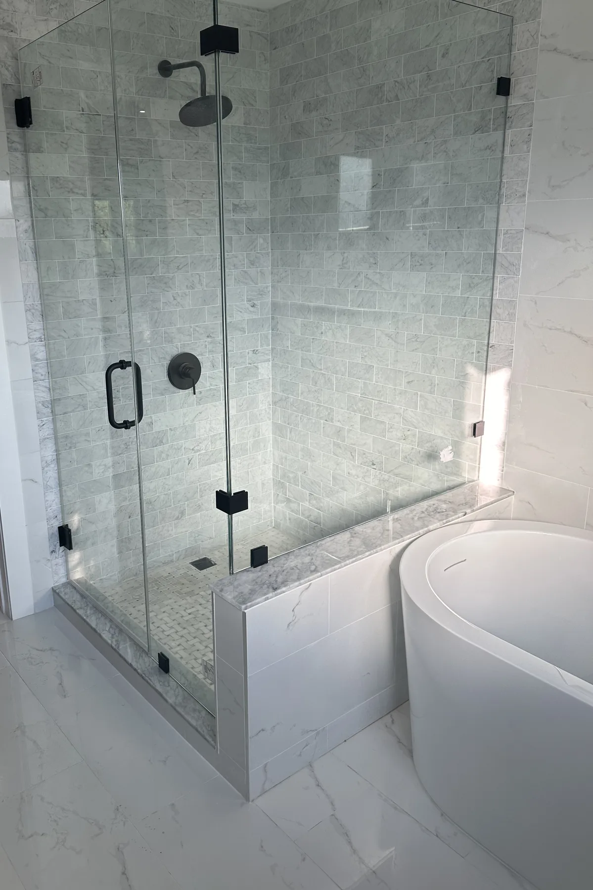 Finished bathroom with a frameless glass shower, black fixtures and white marble-look tile