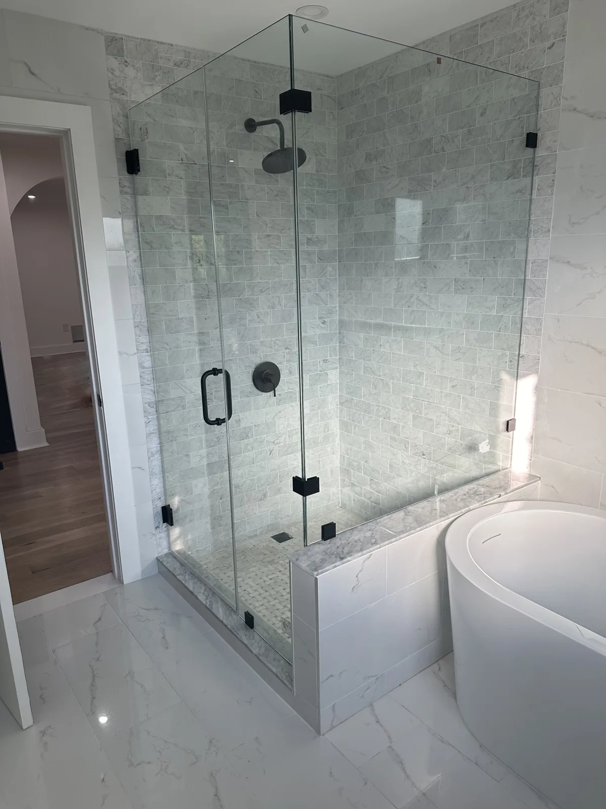 Frameless glass shower with black fixtures next to a freestanding soaking tub