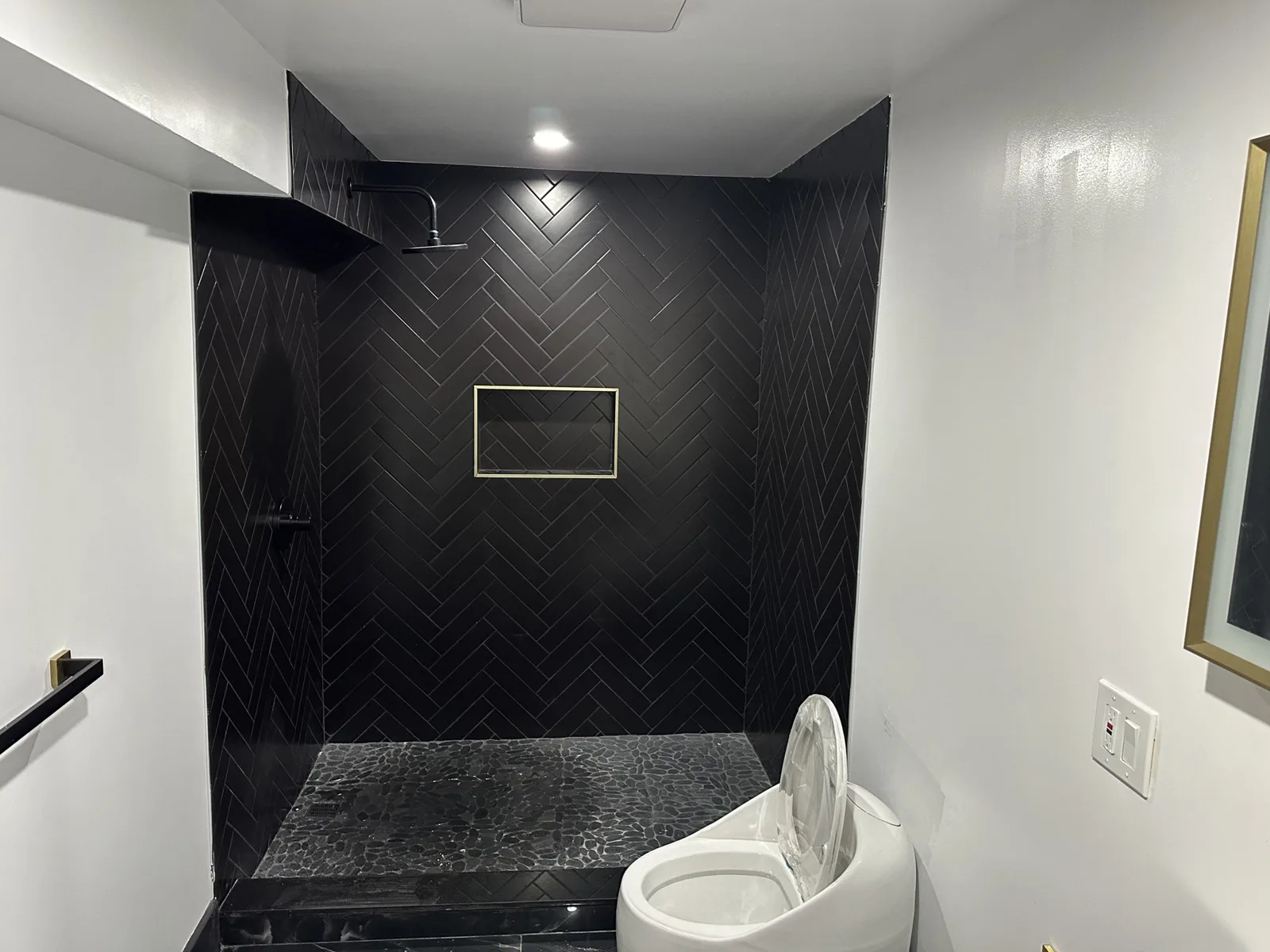 Walk-in shower with black herringbone tile, pebble floor and gold-trimmed niche