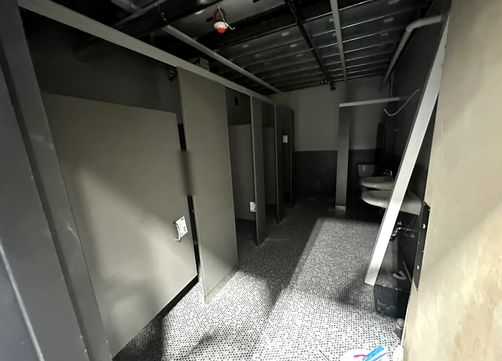 Commercial restroom under construction with gray partitions, penny tile floor and wall sinks