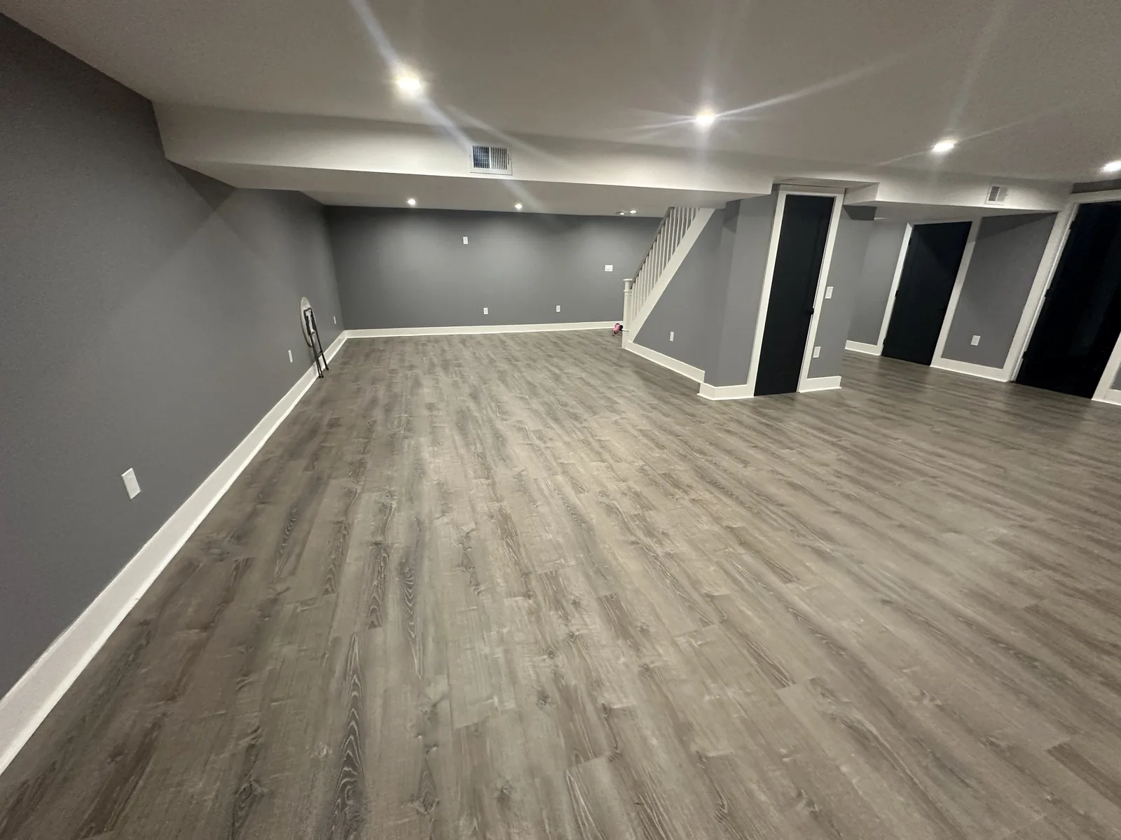 Finished basement with gray walls, white trim, recessed lights, wood-look plank flooring, and a white stair railing