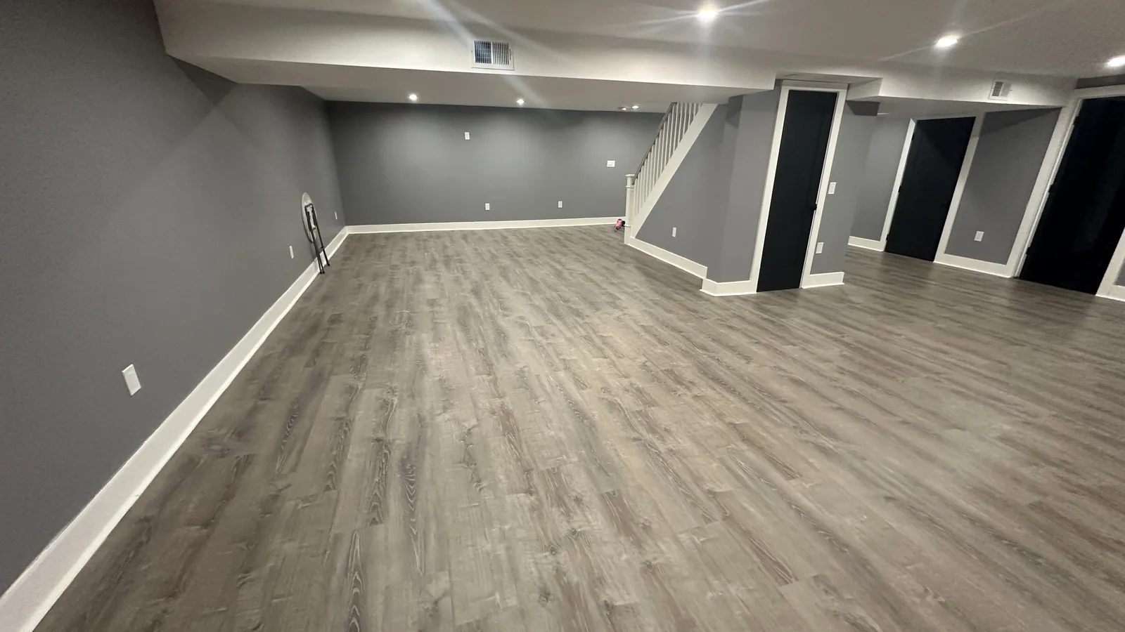 Finished basement with gray walls, white trim, recessed lights, wood-look plank flooring, and a white stair railing