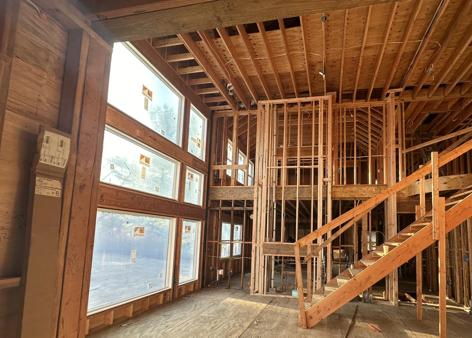 Open wood framing with a two-story stair opening and tall window wall before drywall