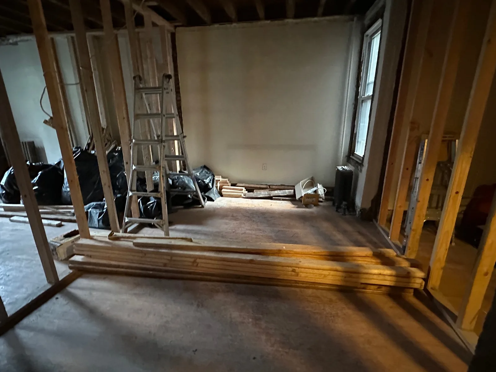 Gutted floor of an older home with new stud walls, exposed ceiling joists, a cast-iron radiator, and lumber stacked on the subfloor