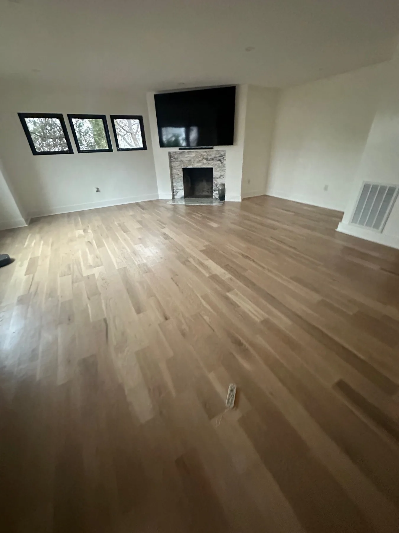 Wide view of the finished living room showing light wide-plank hardwood running the length of the room toward the stone-faced fireplace and black-framed windows