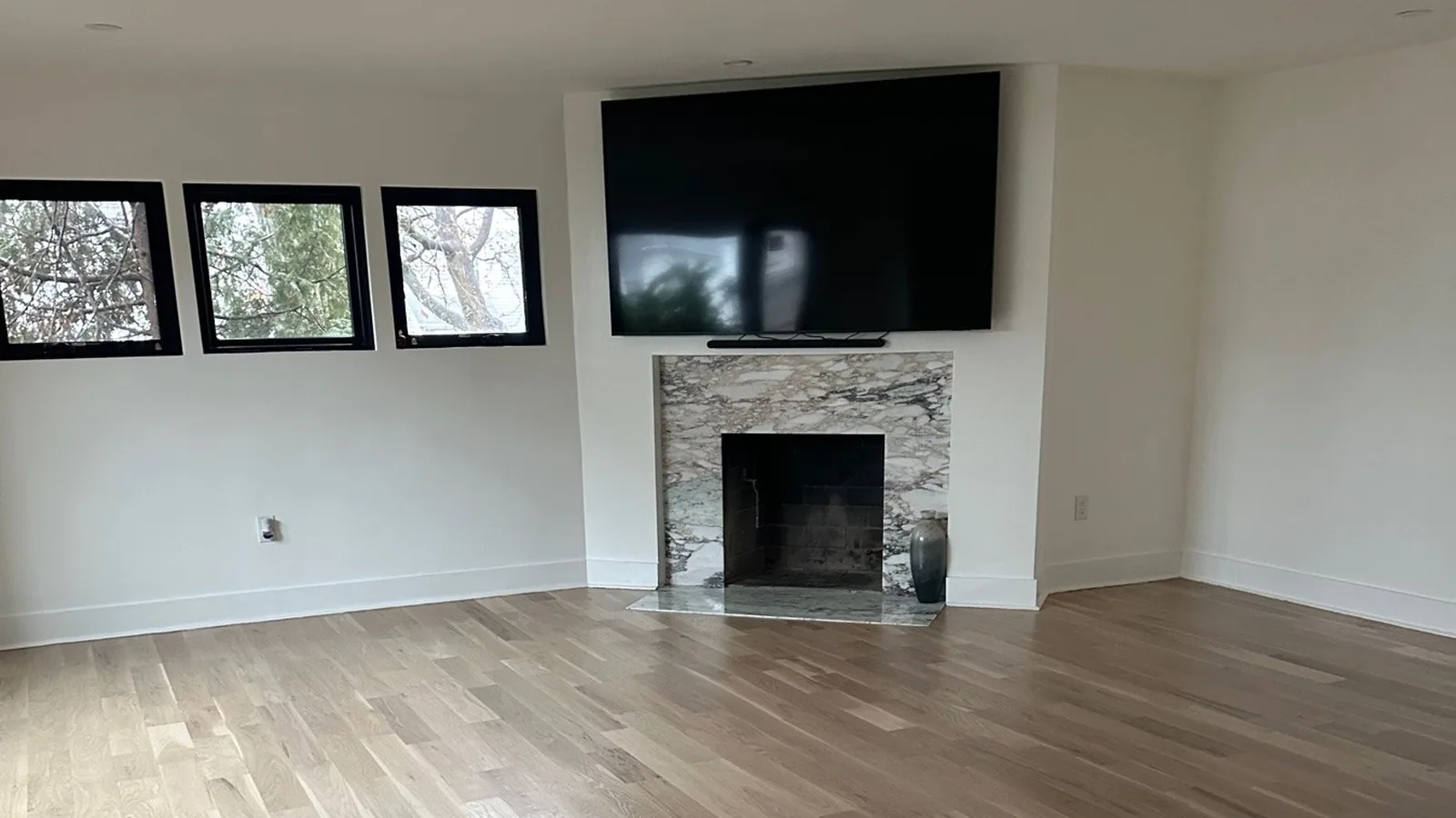 Finished Hackensack, NJ living room with light wide-plank hardwood floors and a gray-veined stone fireplace surround below a wall-mounted TV