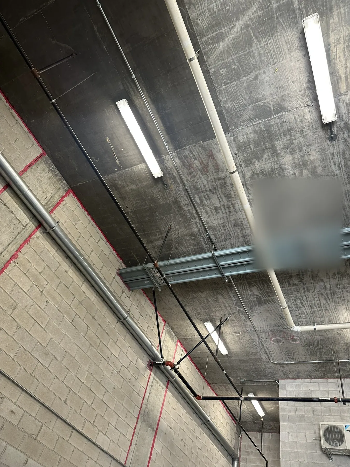 Raw commercial shell with exposed concrete ceiling, block walls and overhead piping