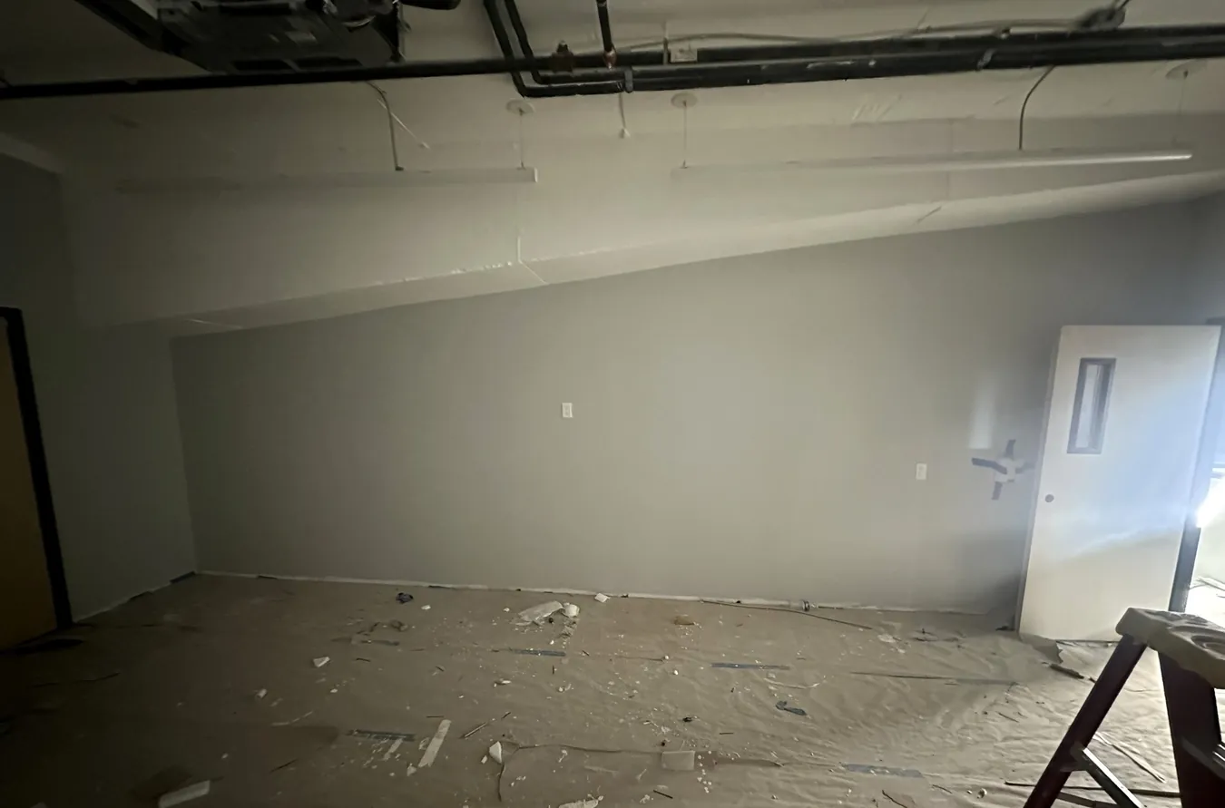 Room with new painted gray walls, a white door, exposed ceiling pipes and paper floor protection