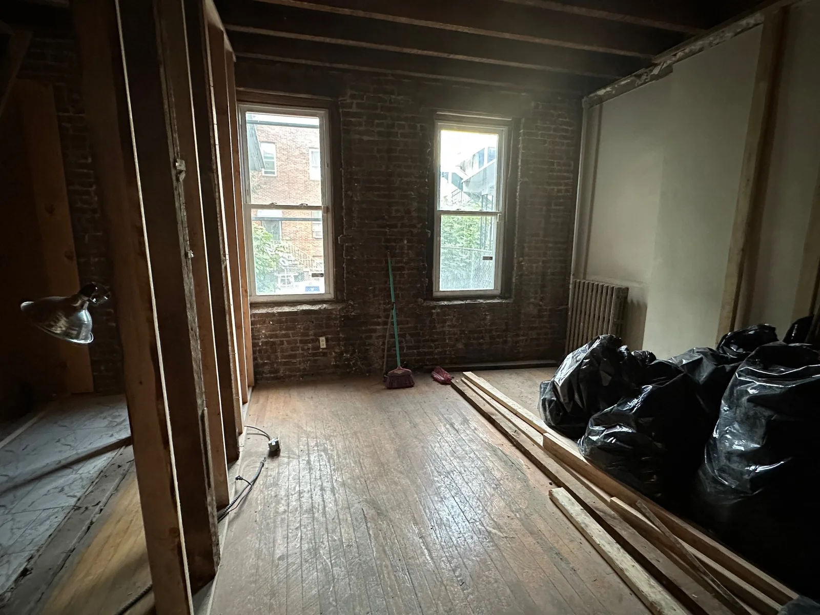 Older brick-walled room taken down to the original wood floor and exposed ceiling joists, with demolition debris bagged in the corner