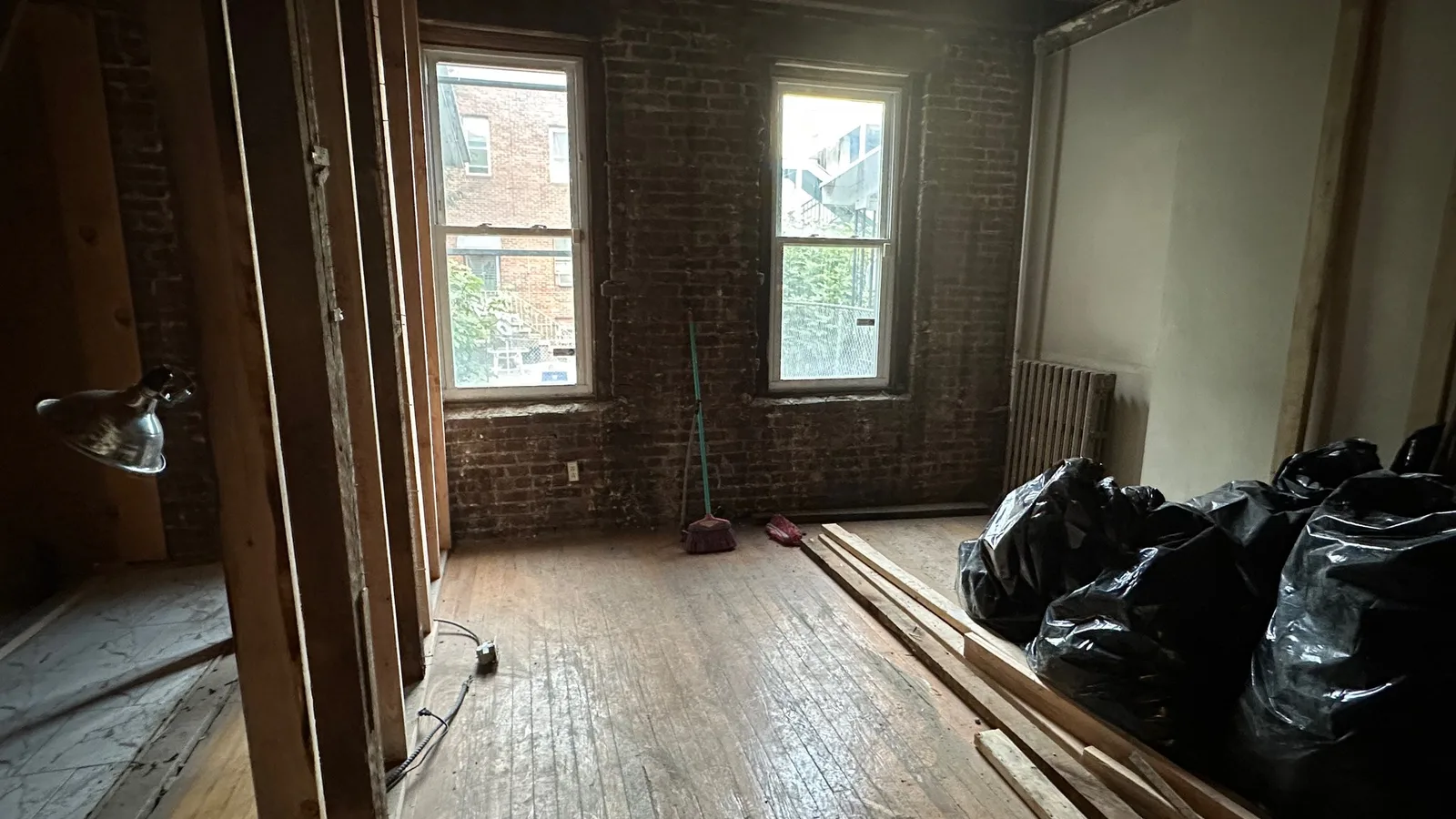 Older brick-walled room taken down to the original wood floor and exposed ceiling joists, with demolition debris bagged in the corner
