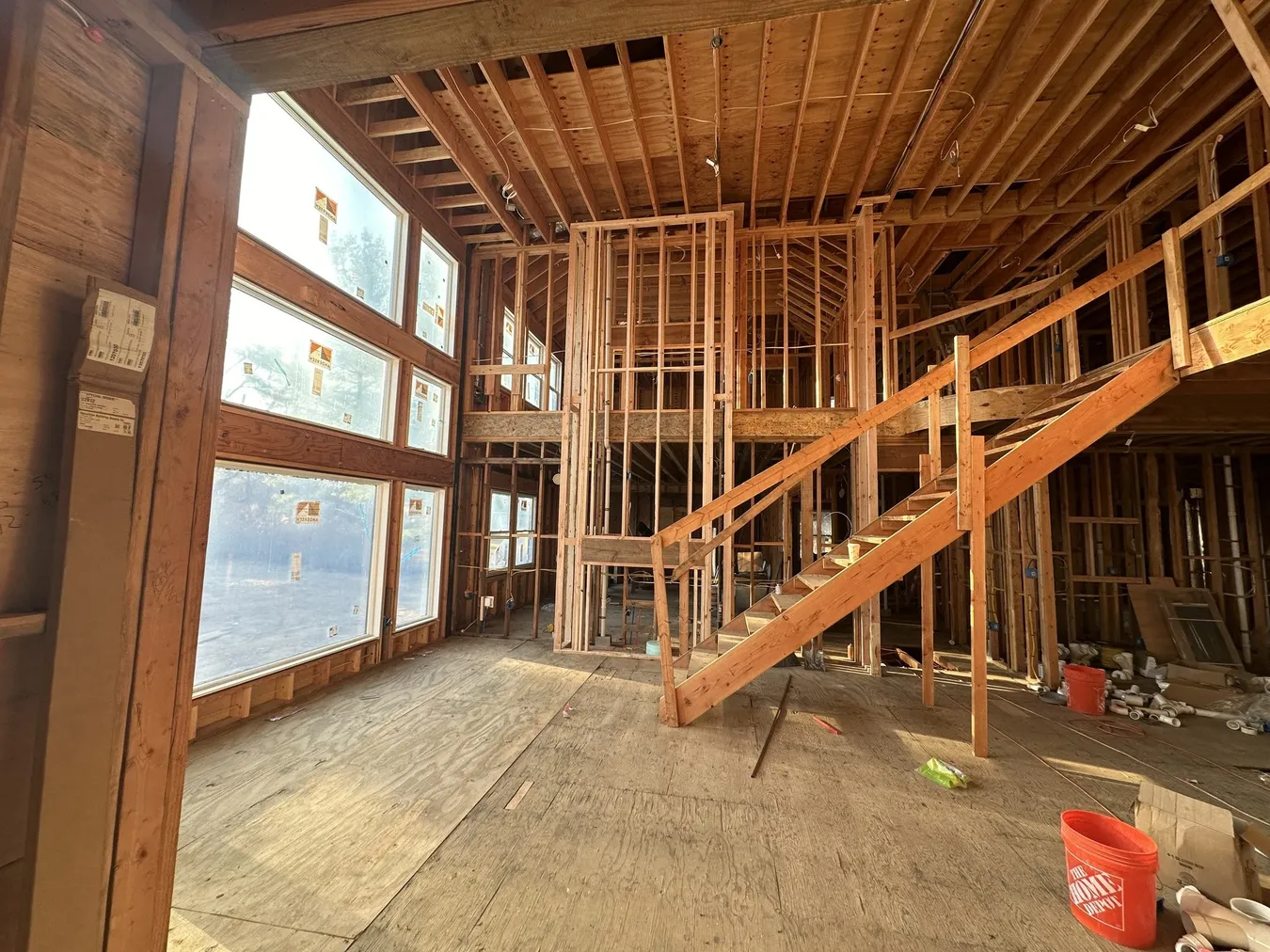 New construction framing with an open staircase, tall windows and exposed roof rafters
