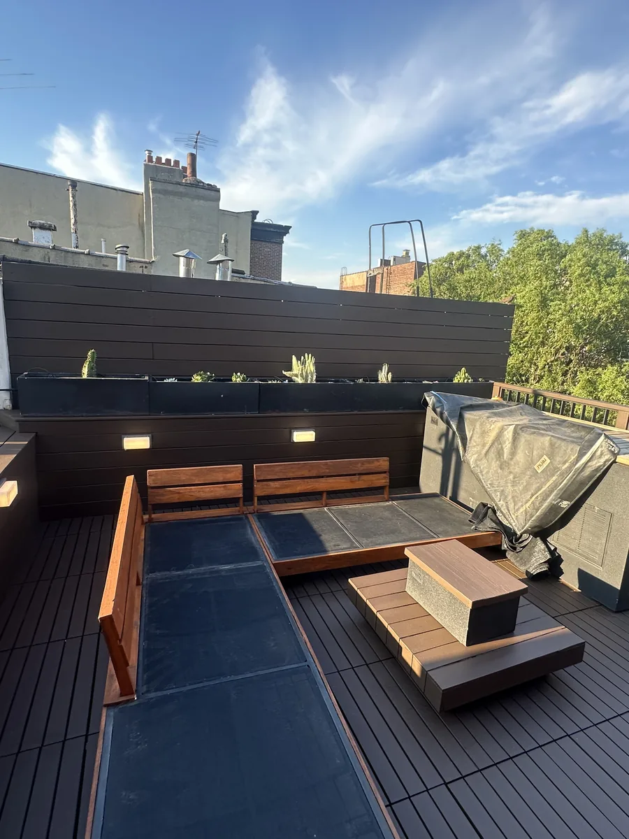 Finished rooftop deck with composite decking, built-in bench seating and planters overlooking Hoboken rooftops