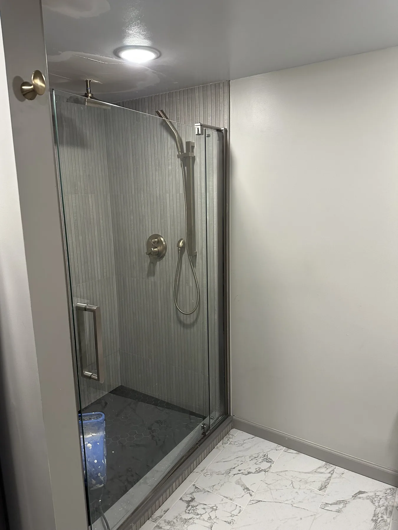 Frameless glass shower door with brass fixtures and fluted grey tile