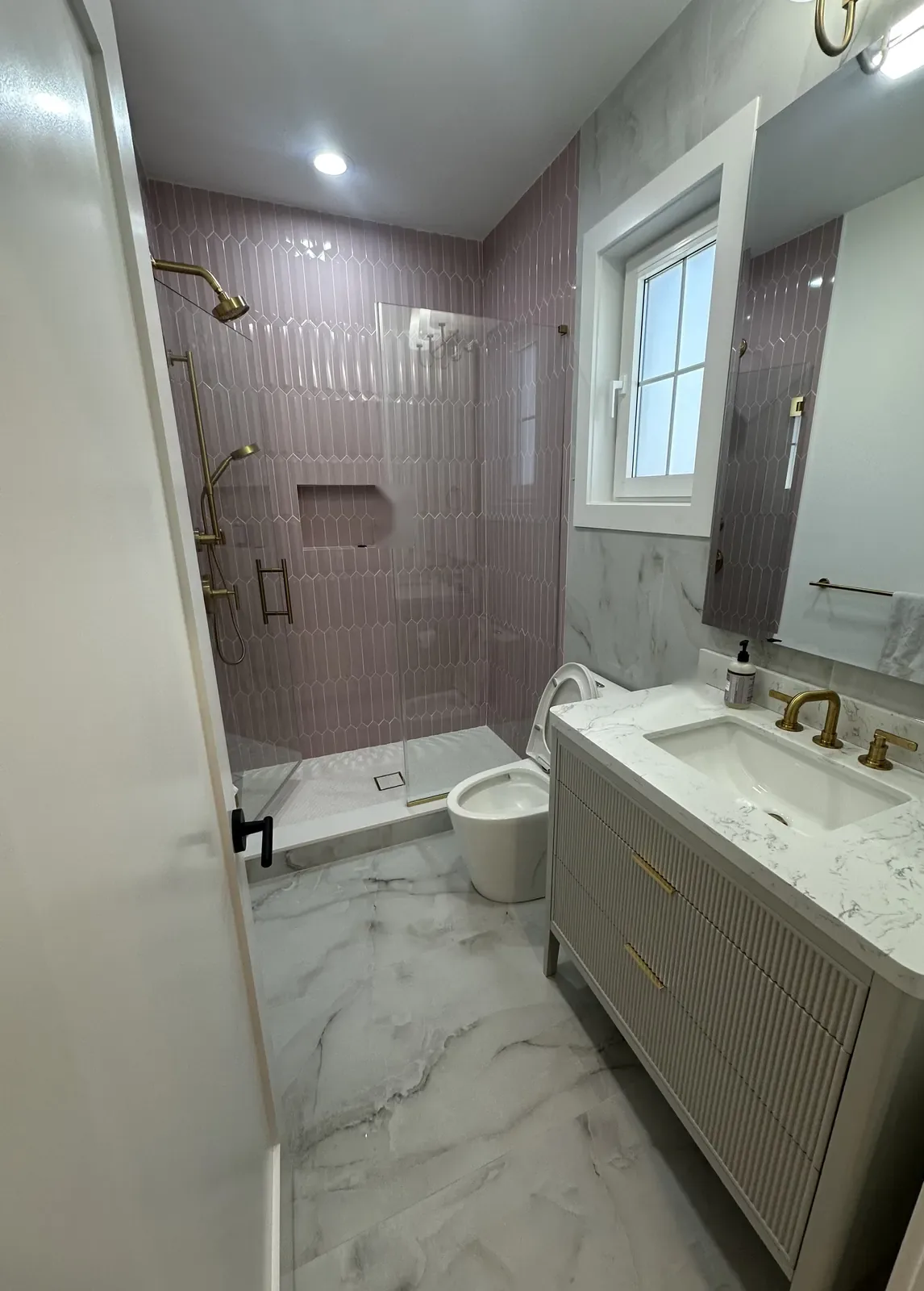 Finished bathroom with a fluted vanity, brass fixtures and a shower in mauve picket tile