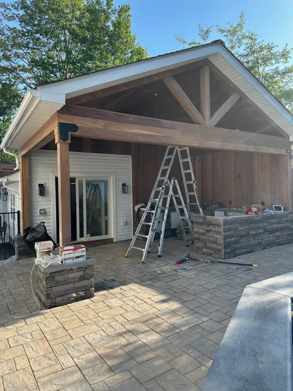 Outdoor kitchen pavilion under construction in Lake Hiawatha, NJ: cedar ceiling, stone-veneer counters and paver patio with ladders on site