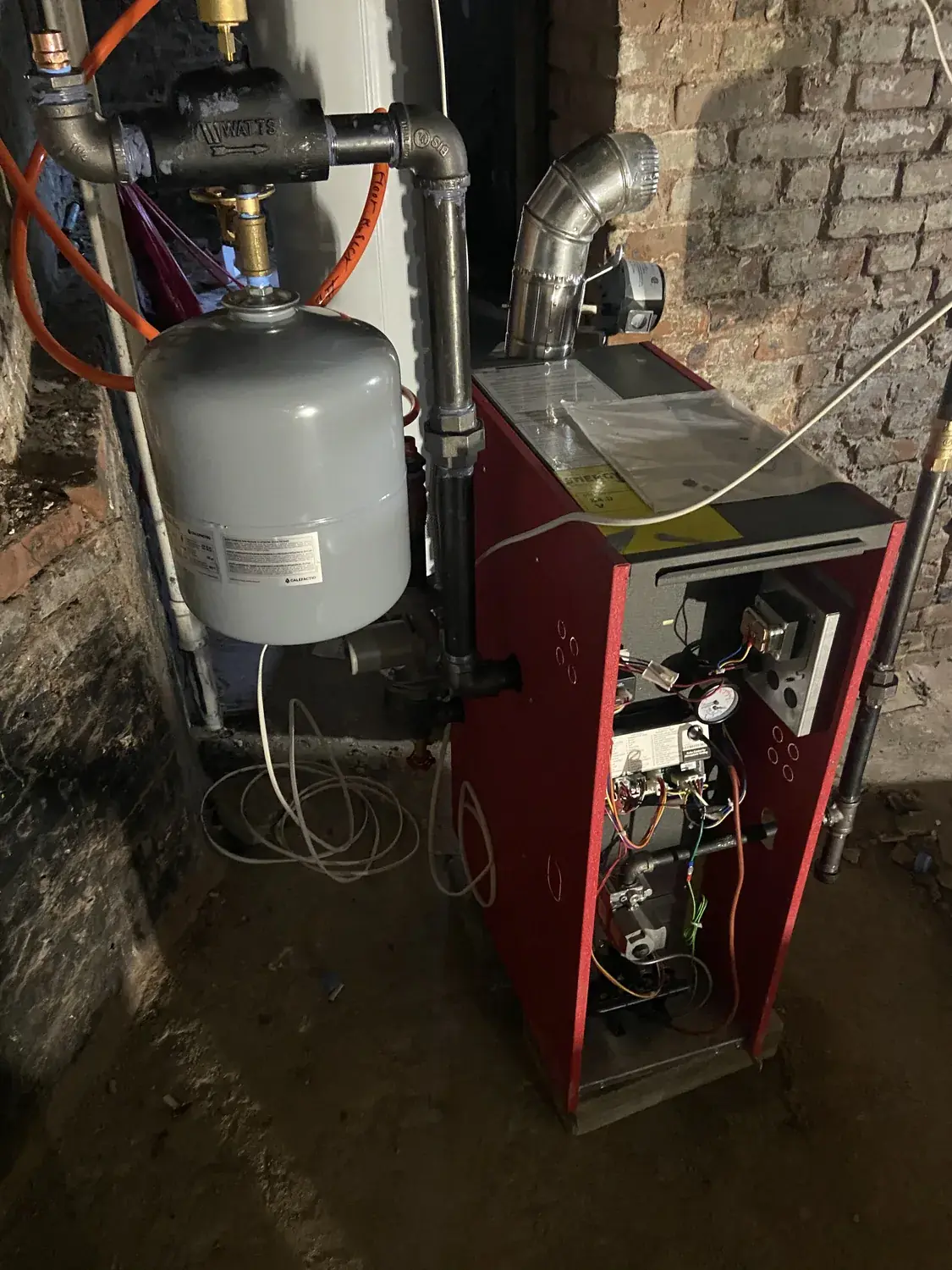 Gas boiler installation in progress with black iron gas piping and an expansion tank against a brick basement wall