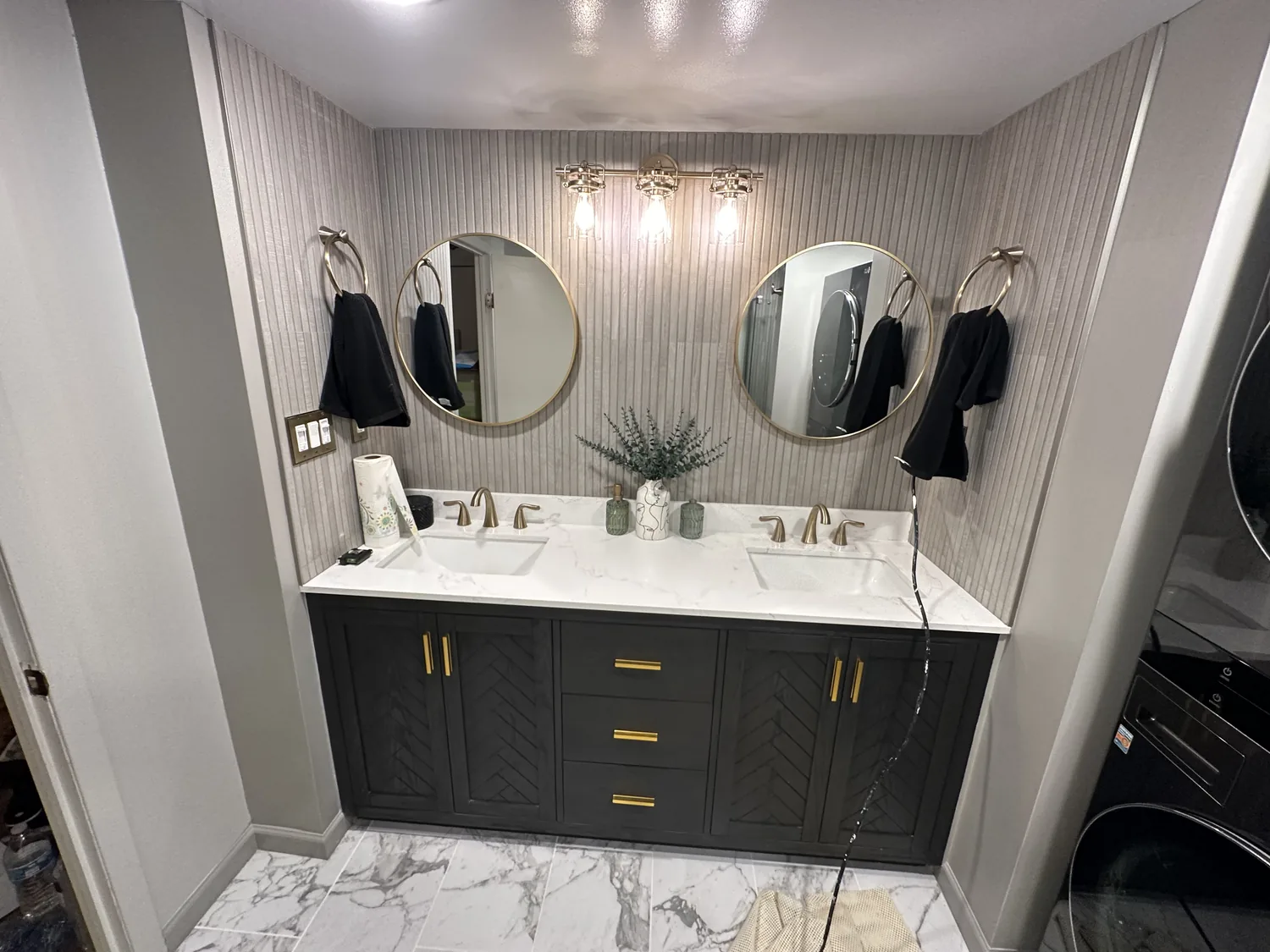 Double vanity with chevron-pattern doors, brass pulls, round mirrors and fluted wall tile