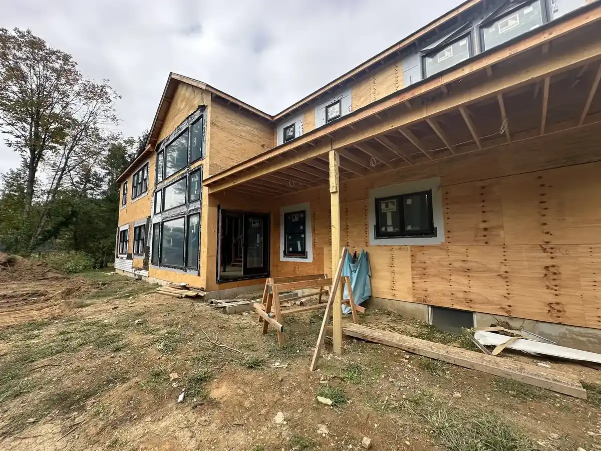 New construction house sheathed and weather-tight with black-framed windows and a covered porch, ready for siding