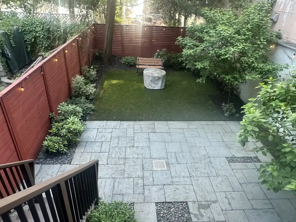 Brownstone rear yard with a paver patio, turf lawn, planting beds and a painted privacy fence