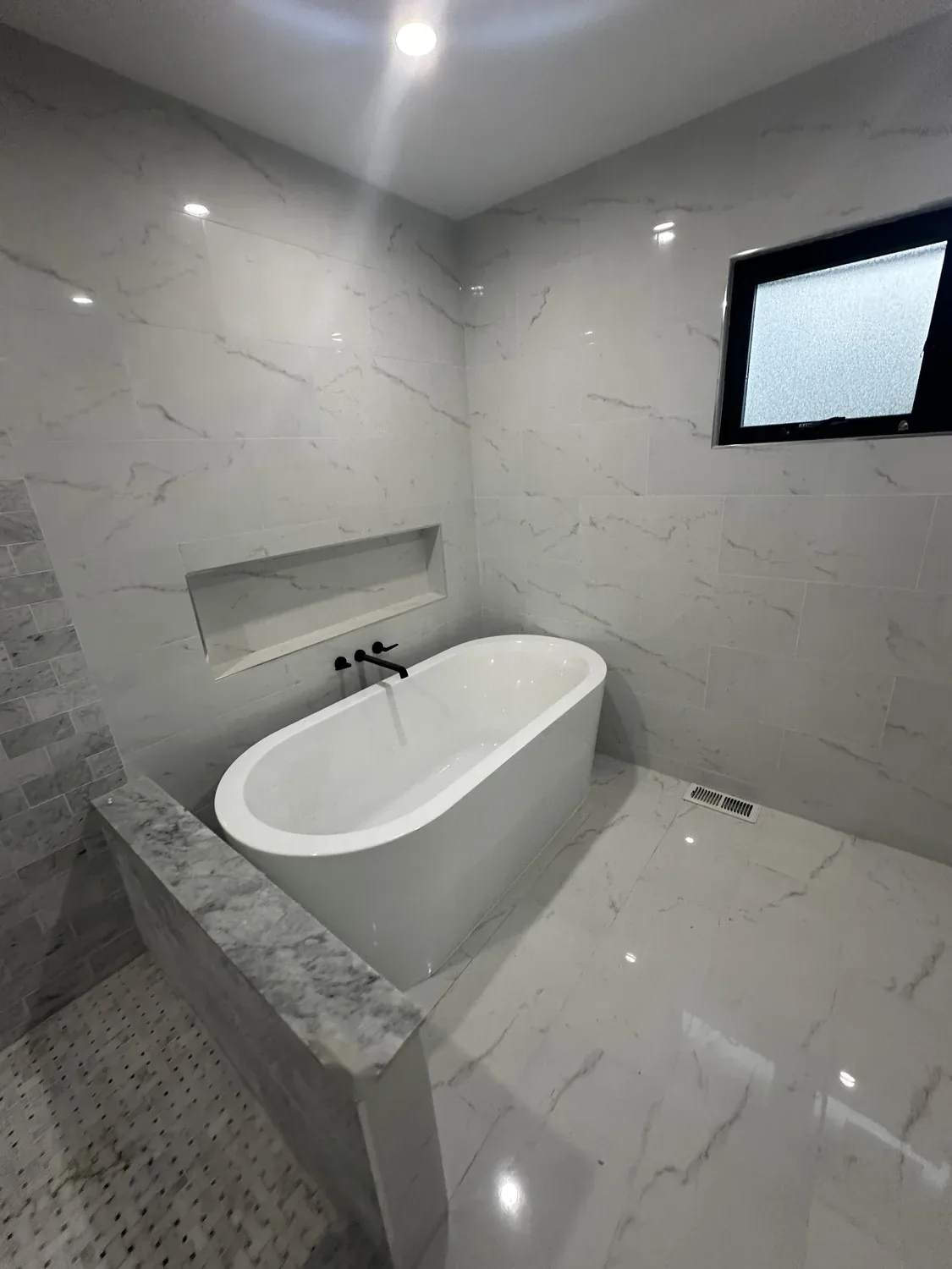 Finished primary bathroom with a freestanding soaking tub, wall-mounted matte black filler and marble-look tile in Hackensack, NJ