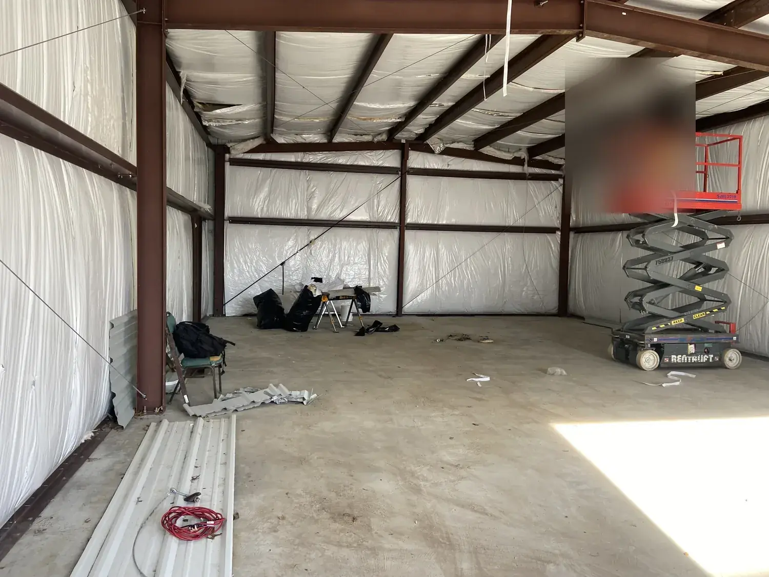 Structural steel frame building interior in progress with insulated wrap and a scissor lift