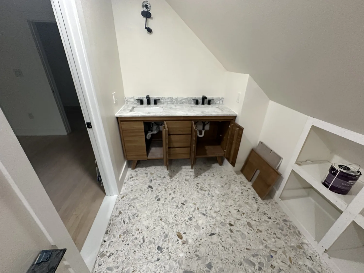 Attic bathroom build-out in progress with terrazzo floor tile, a wood double vanity and built-in white shelving under a sloped ceiling